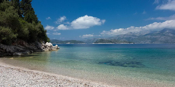 Une plage typique de la Croatie : eau limpide, petits galets avec vue sur les montagnes environnantes.